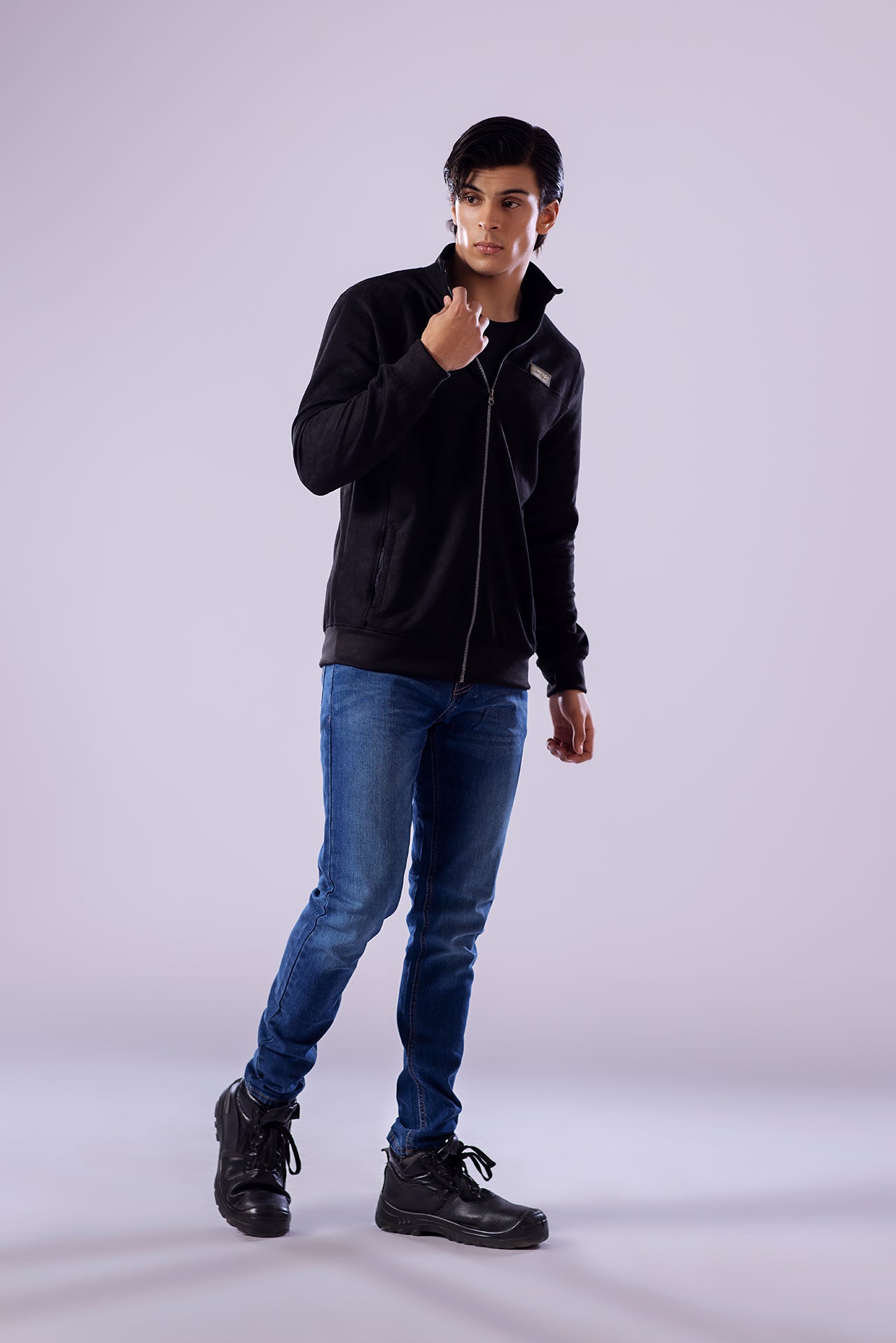 Person wearing a black jacket, blue jeans, and black shoes on a white background