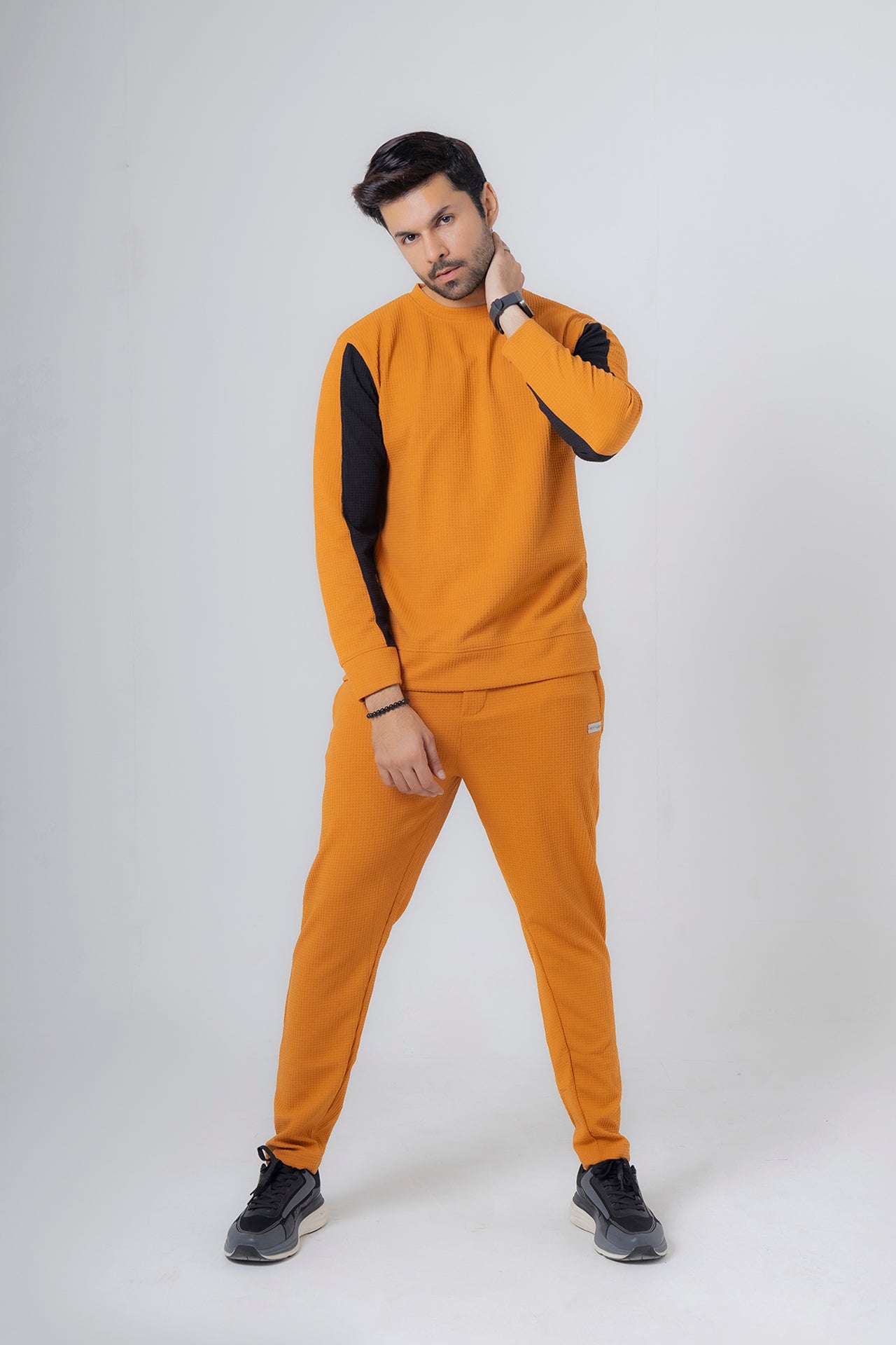 Man wearing a mustard yellow tracksuit with black sleeves on a white background