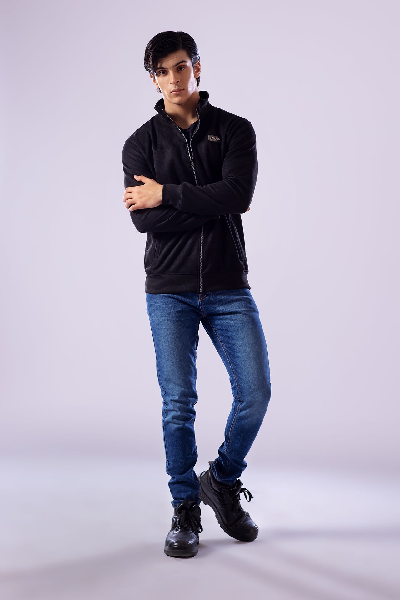 Person wearing a black jacket, blue jeans, and black shoes on a light gray background