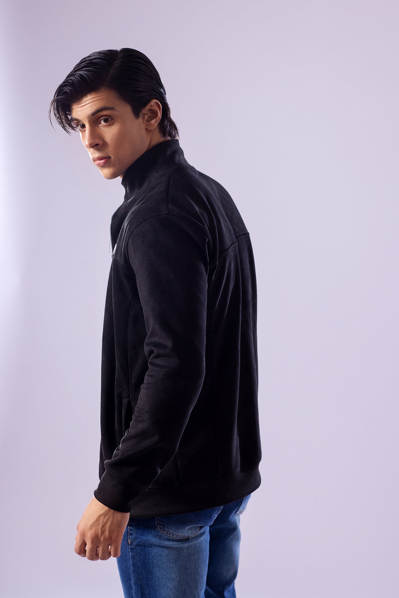 Man wearing a black jacket and blue jeans against a light gray background