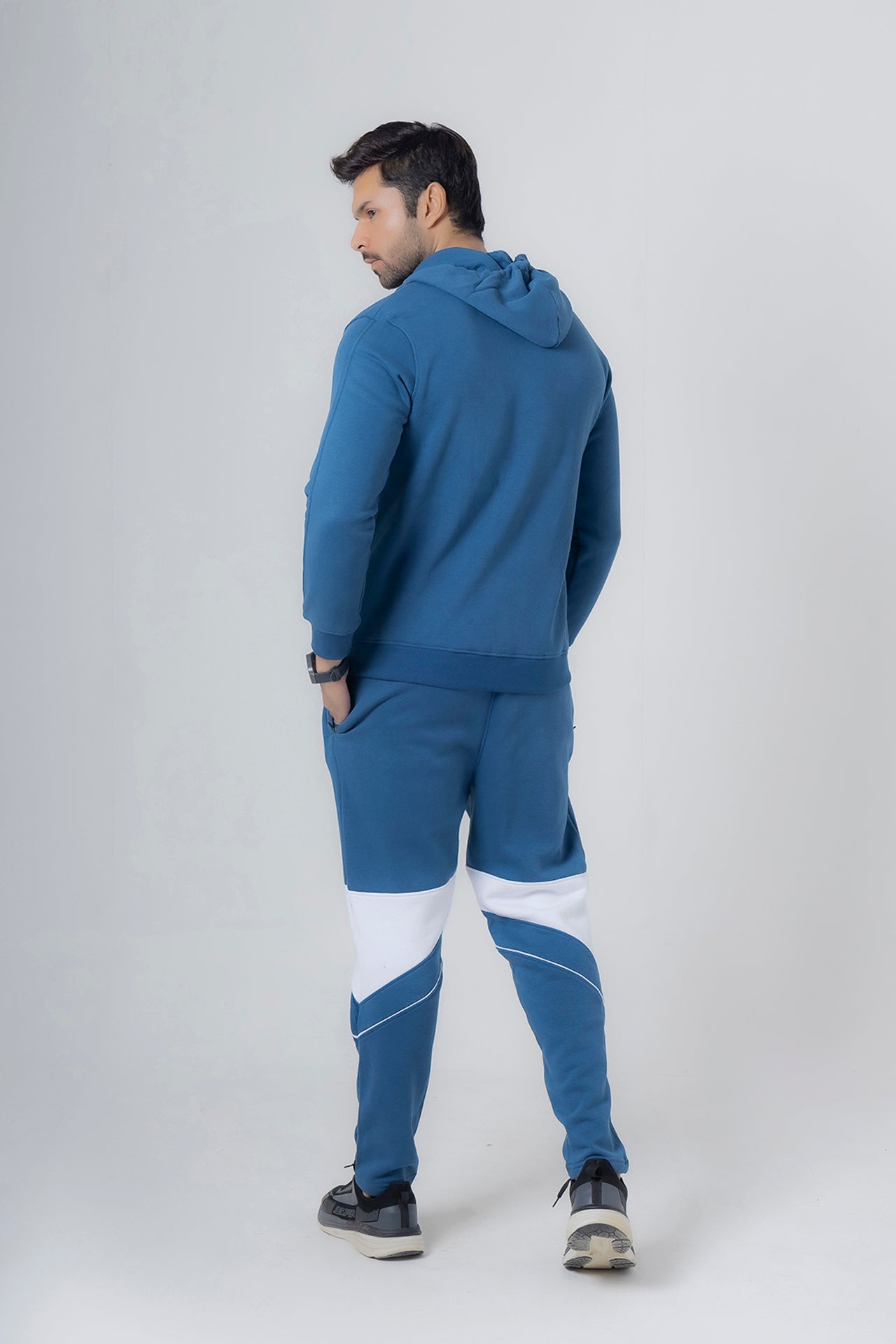 Man wearing a blue tracksuit with white accents on a light gray background