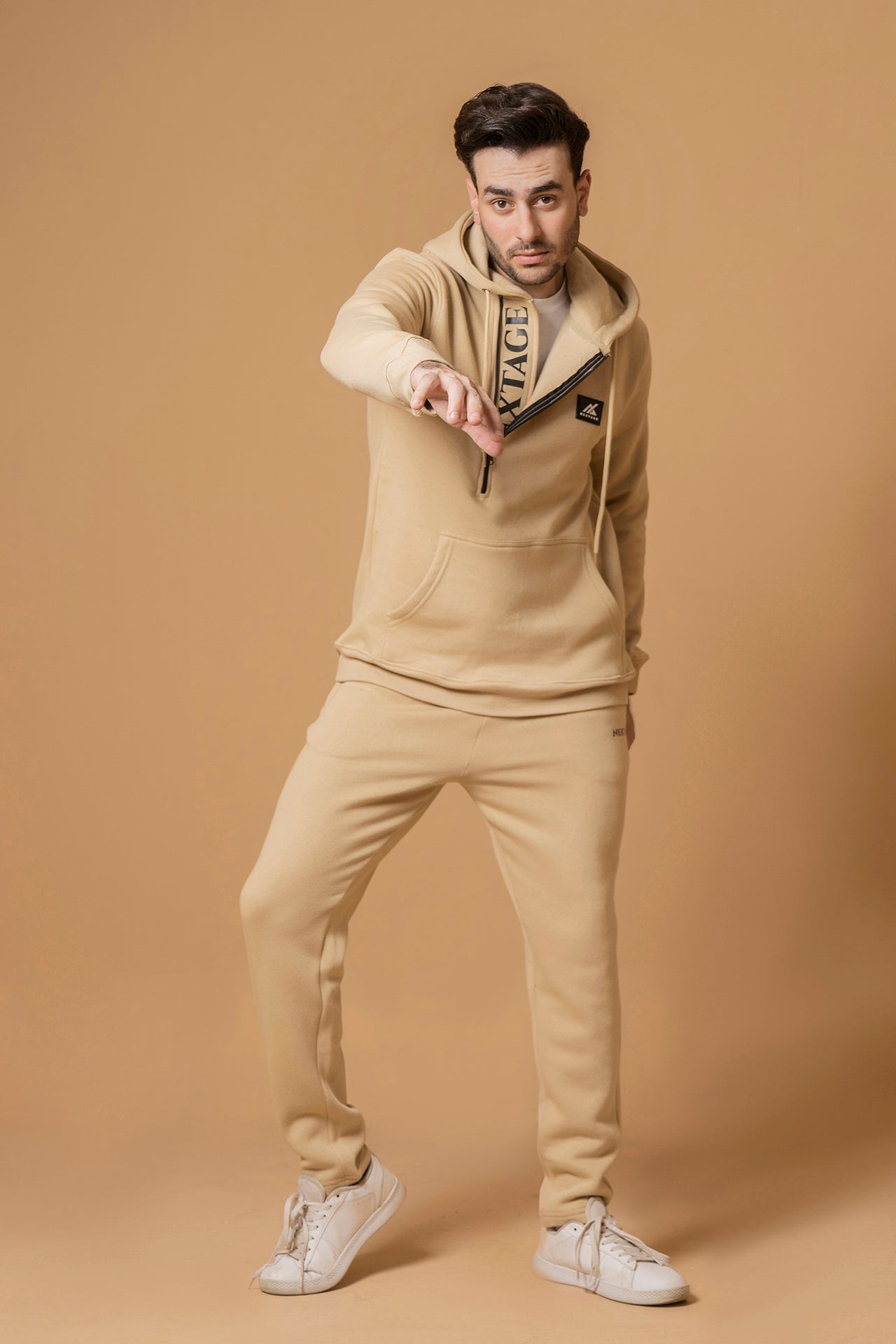Nextage Model wearing a beige tracksuit with a brand logo on a brown background