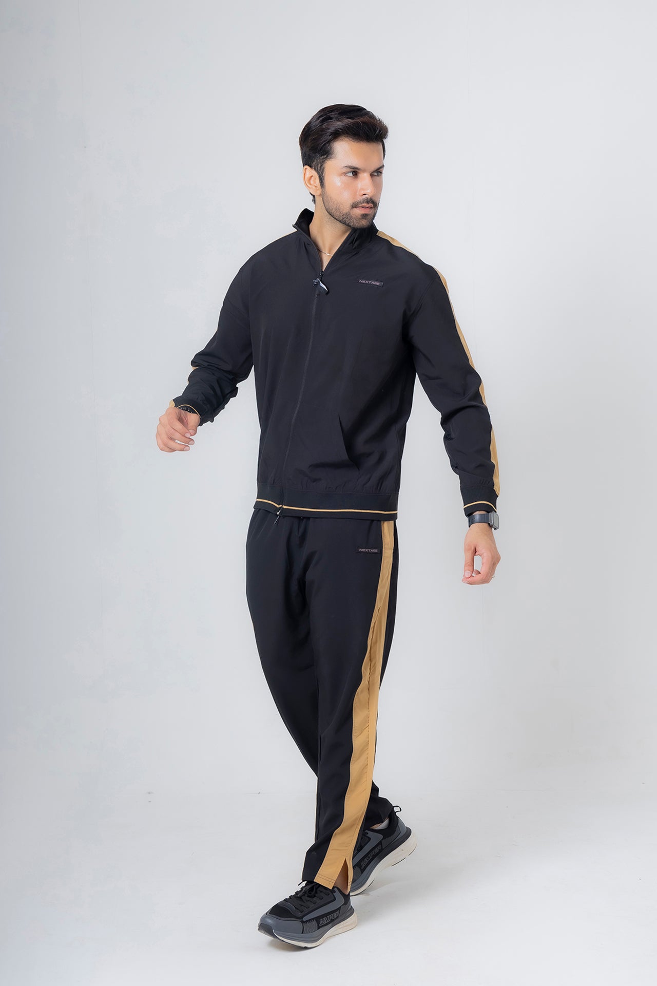 Man wearing a black tracksuit with gold accents on a white background