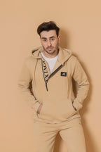 Man wearing a beige tracksuit with a logo on a beige background