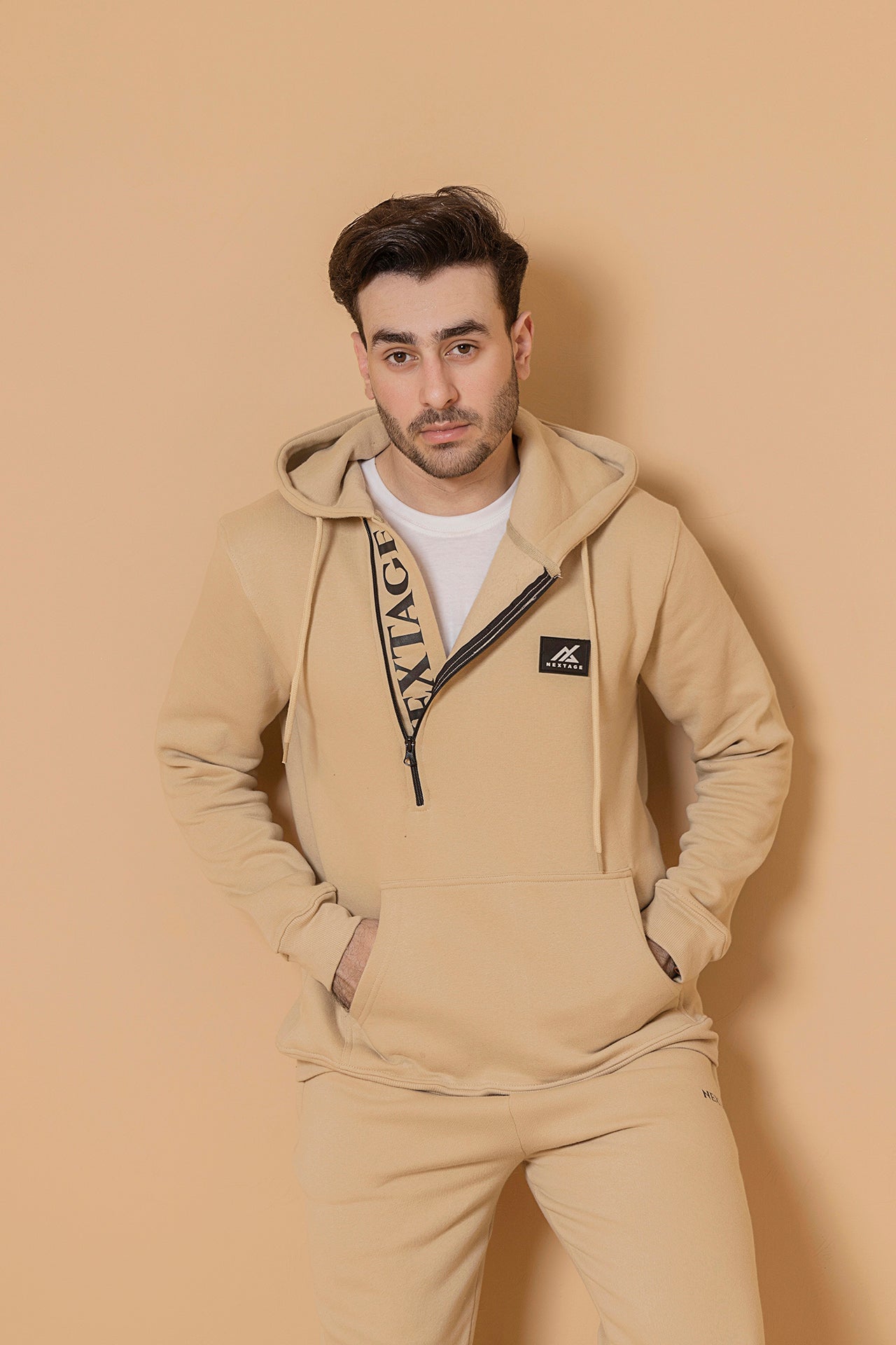 Man wearing a beige tracksuit with a logo on a beige background