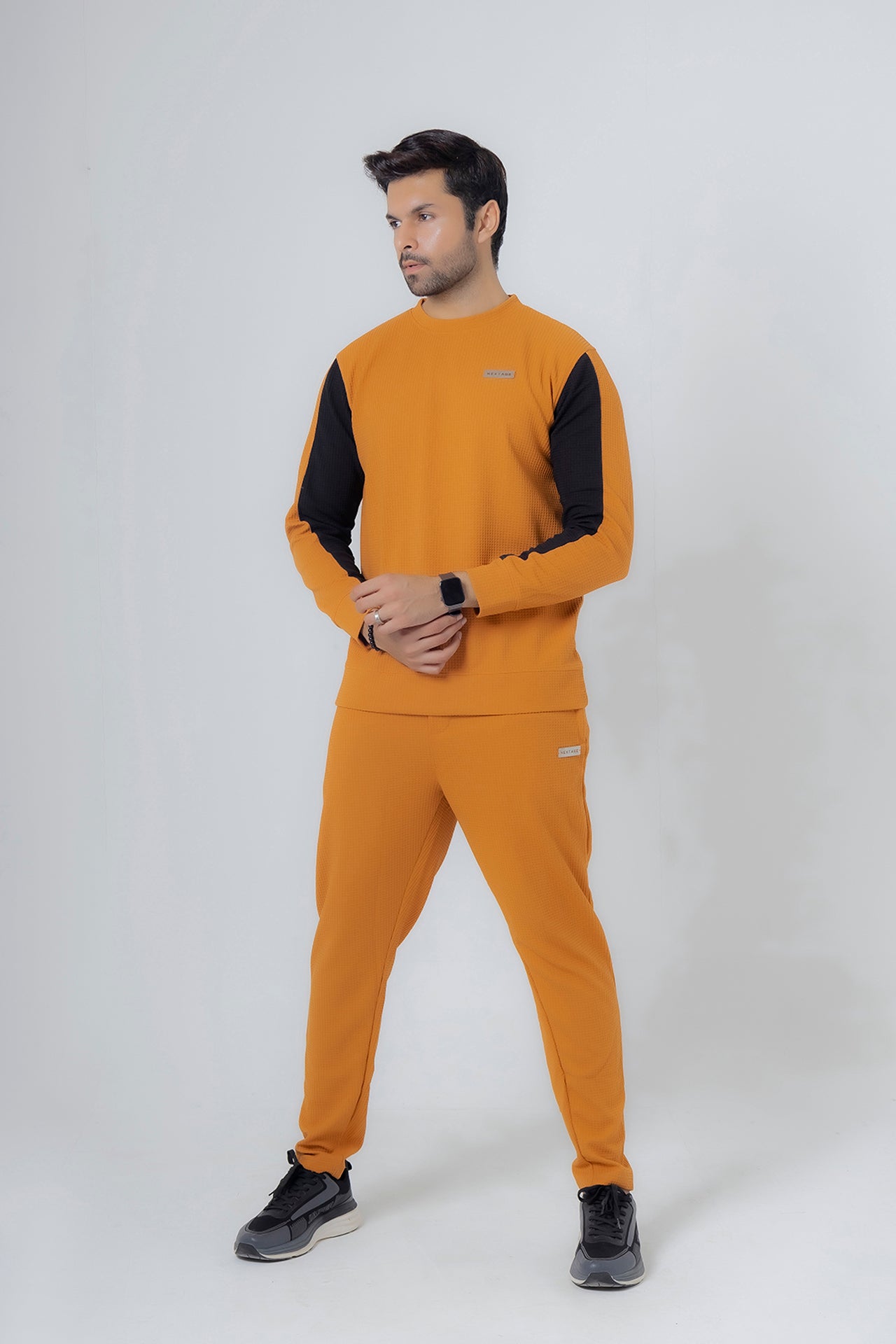 Man wearing a mustard yellow tracksuit with black sleeves on a white background