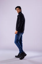 Man wearing a black turtleneck, blue jeans, and black shoes on a white background