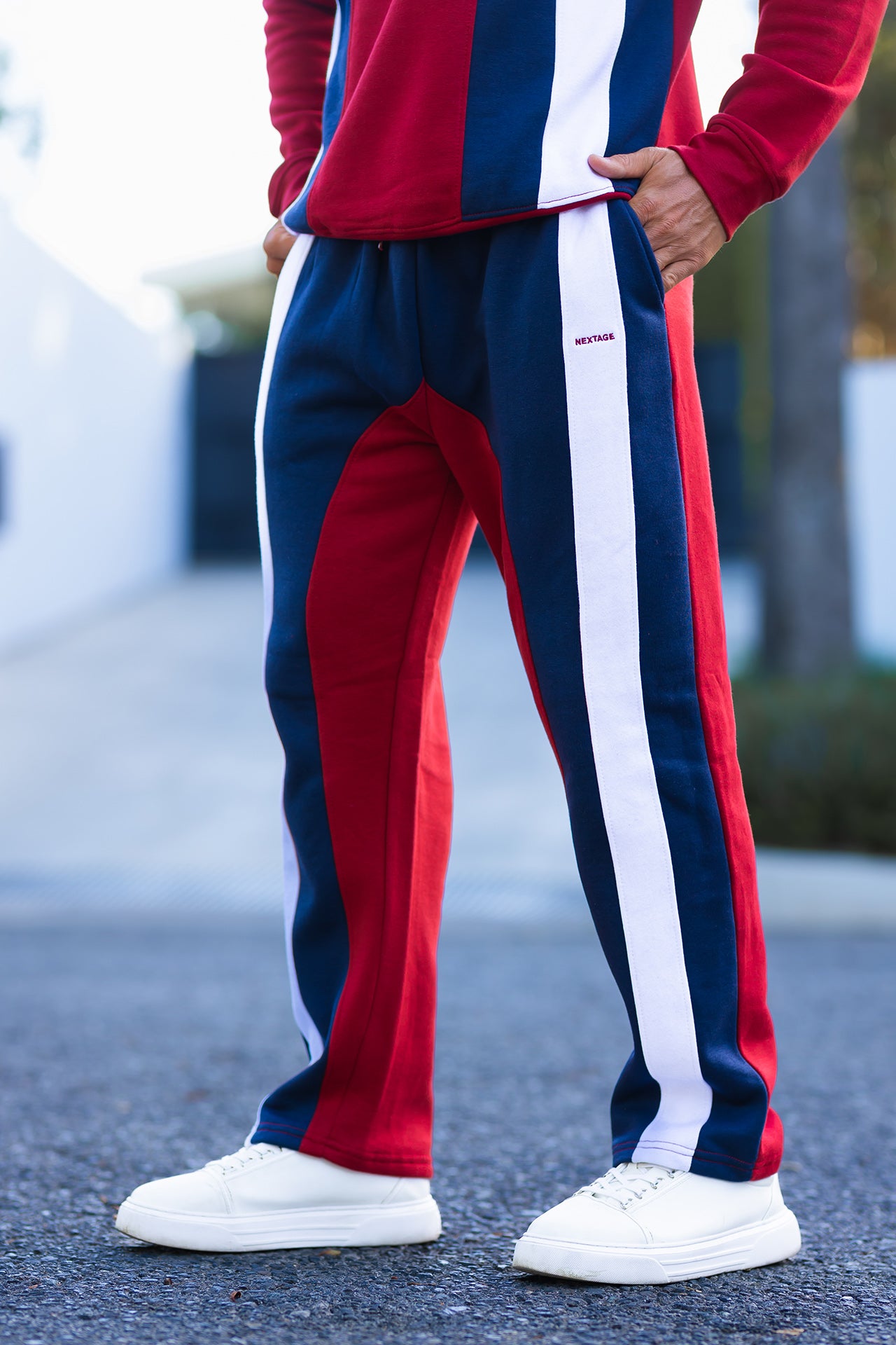 Nextage Person wearing a red, white, and blue striped tracksuit with white sneakers on a blurred outdoor background.