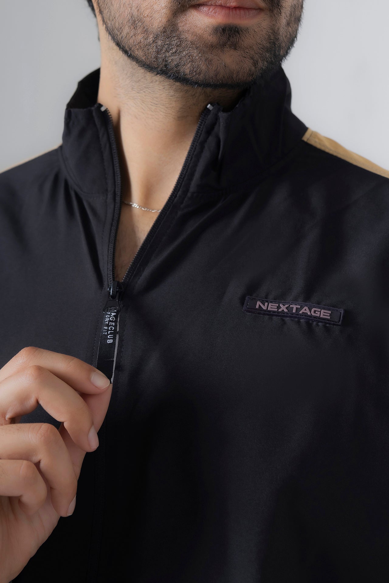 Person wearing a black jacket with 'NexTage' branding on a neutral background