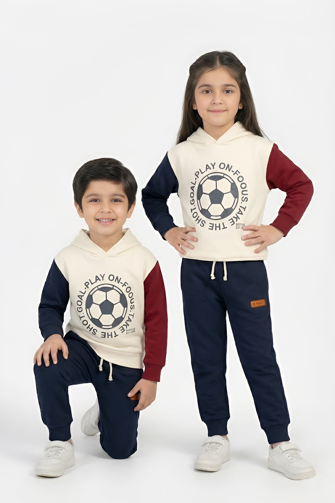 Two children wearing matching outfits with soccer-themed hoodies and pants on a white background.
