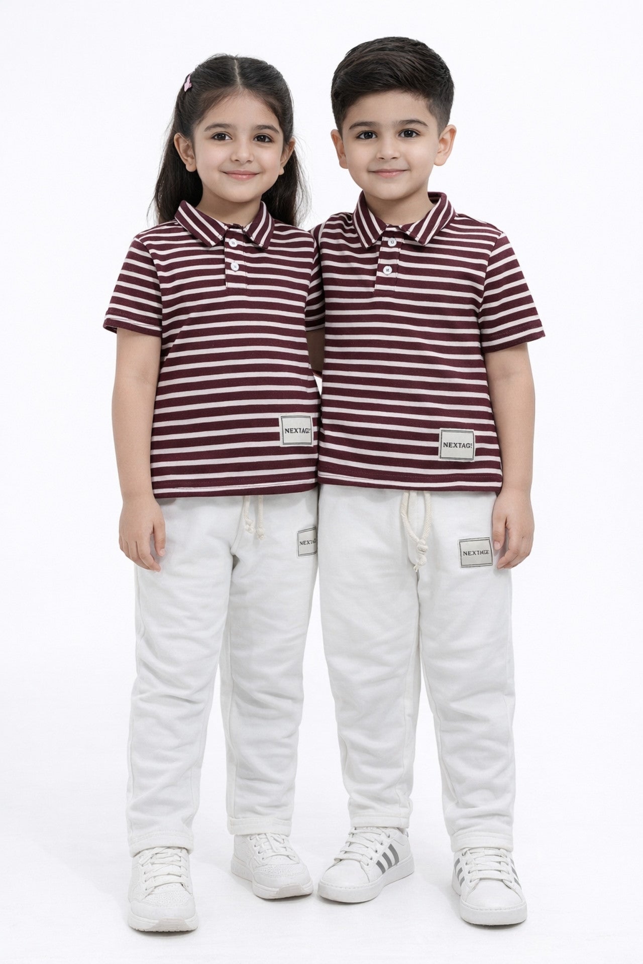 Two children wearing matching striped polo shirts and white pants on a white background