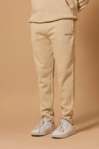 Person wearing beige sweatpants with 'Hextage' branding on a beige background