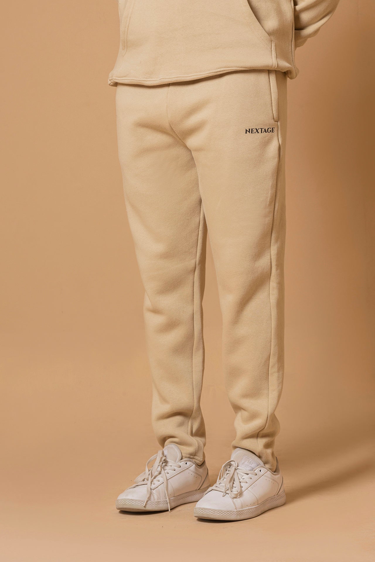 Person wearing beige sweatpants with 'Hextage' branding on a beige background