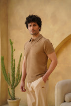 Man wearing a beige polo shirt and pants standing in a warm-toned room with a cactus plant.