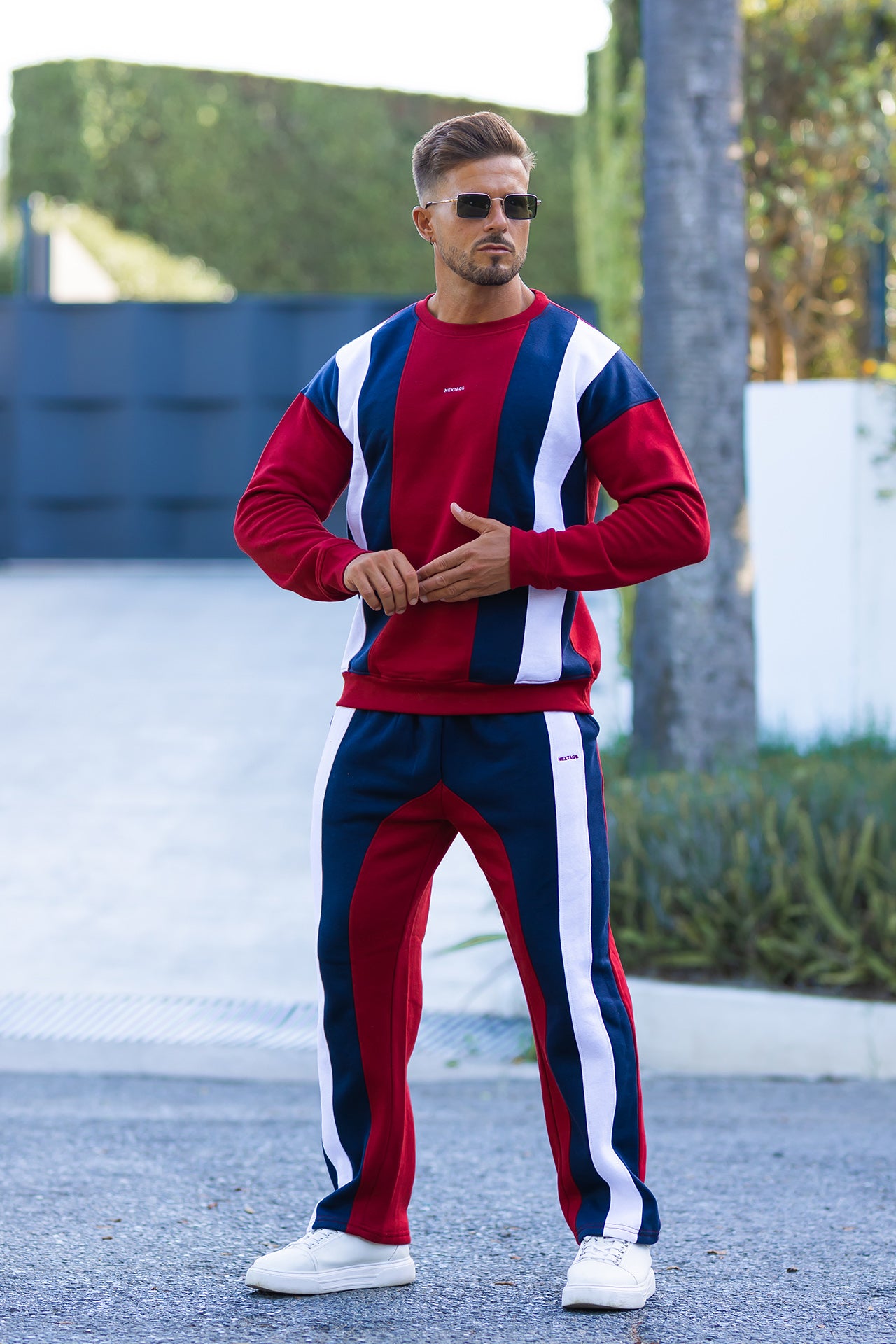 Nextage Model wearing a Burgundy, white, and Navy tracksuit with sunglasses outdoors.